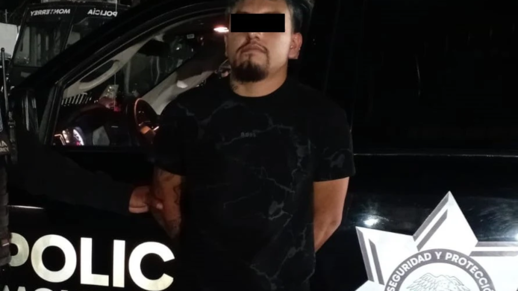 Man in a Black Shirt Stands Beside a Dark Police Suv at Night; a Officer's Hand is on His Arm While His Eyes Are Obscured by a Black Bar. - Cambiando Mty