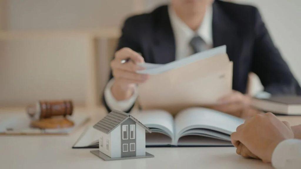 Lawyer in a Suit Reviewing Documents with a Small House Model on the Desk, Symbolizing Real Estate Legal Advice. - Cambiando Mty