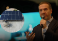 Speaker in a dark suit speaks into a microphone on stage; circular inset shows rooftop solar panels and a storage tank for solar energy.