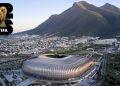 Aerial view of a modern silver stadium beside a city and green hills, with a FIFA World Cup logo in the top-left corner.
